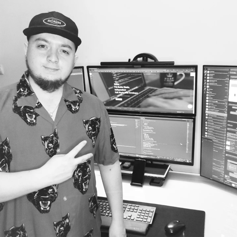 Web developer Sasha Zimin stands in front of his workplace with four monitors, a Bluetooth keyboard, a mouse and a phone stand.